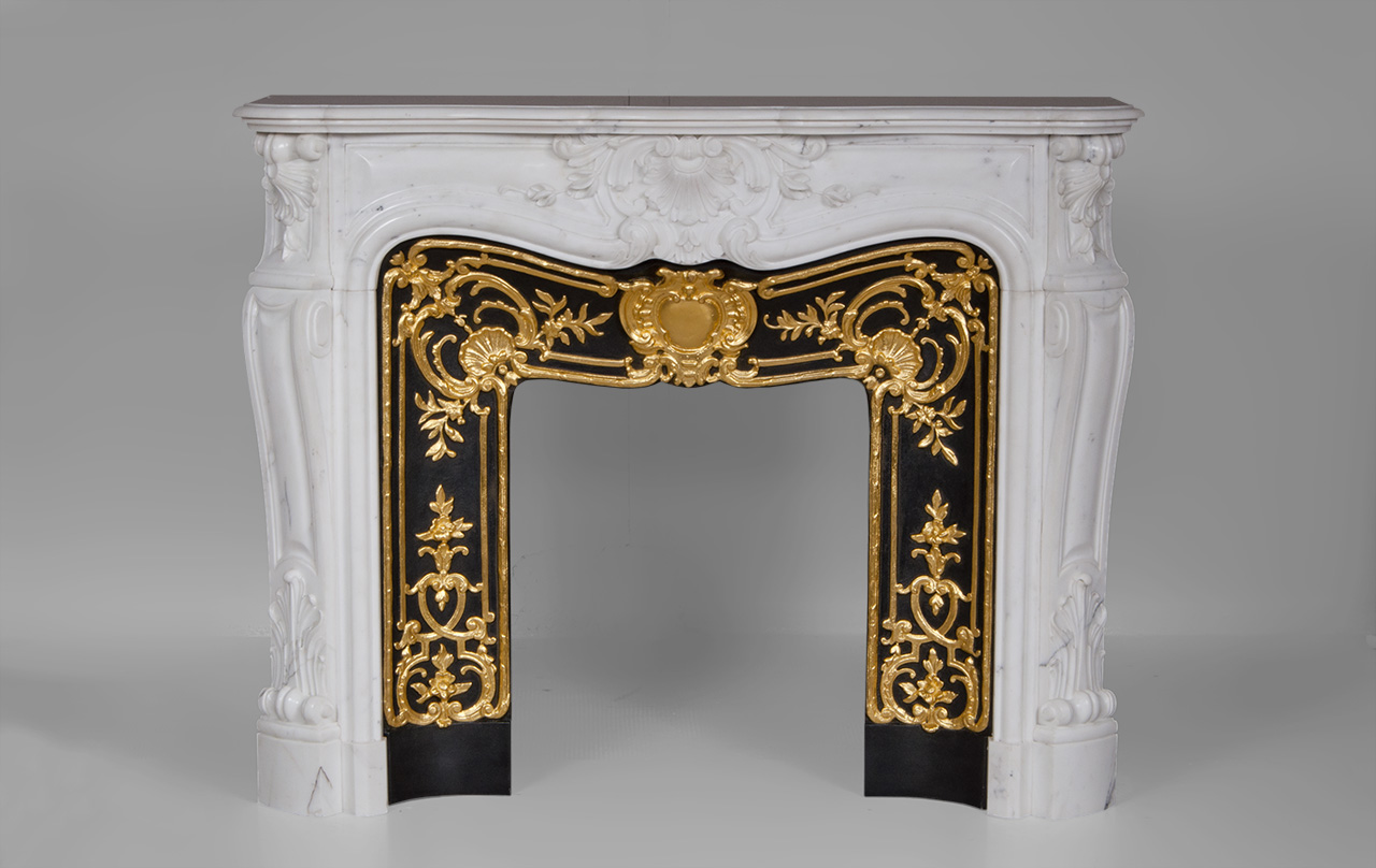 «Madame Du Barry» est une cheminée de style Louis XV en marbre Blanc de Carrare d’une rare opulence.
Les formes généreuses sont richement décorées de motifs végétaux finement sculptés. Le centre du bandeau de cette cheminée sur mesure est orné d’une large coquille fleurie, motif que nous retrouvons sur les têtes de jambages. Ces derniers, aux formes galbées, dessinent un enroulement dans leur partie haute.
