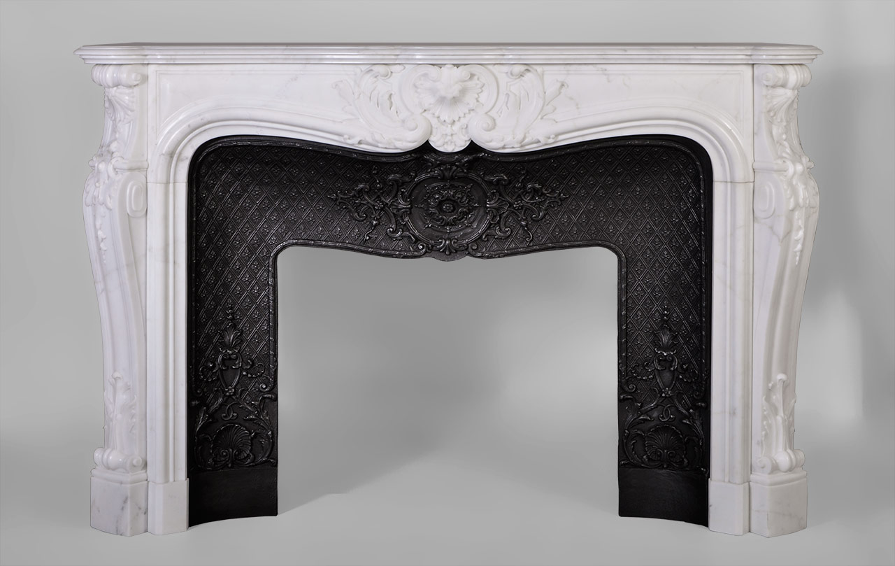 De style Louis XV, le décor sculpté de cette cheminée est extrêmement travaillé. Une grande coquille renversée et feuillagée orne le centre du bandeau. Les jambages au galbe prononcé présentent un enroulement garni d'une feuille d'acanthe charnue dans leur partie basse. Les têtes des jambages sont sculptés de coquilles et clochettes en chute.
Cette cheminée est pourvue d'un bel intérieur en fonte orné de rinceaux, coquilles et médaillons de feuillages sur une fine résille.
 