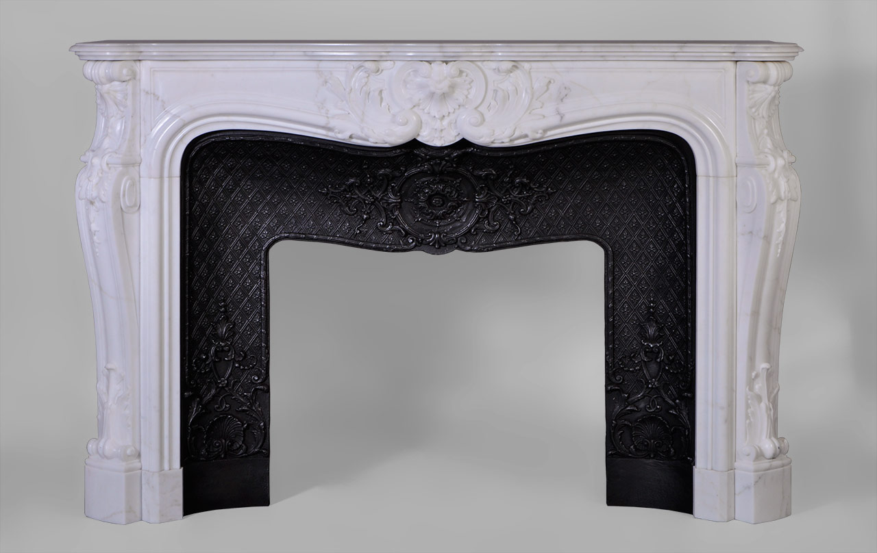 De style Louis XV, le décor sculpté de cette cheminée est extrêmement travaillé. Une grande coquille renversée et feuillagée orne le centre du bandeau. Les jambages au galbe prononcé présentent un enroulement garni d'une feuille d'acanthe charnue dans leur partie basse. Les têtes des jambages sont sculptés de coquilles et clochettes en chute.
Cette cheminée est pourvue d'un bel intérieur en fonte orné de rinceaux, coquilles et médaillons de feuillages sur une fine résille.
 